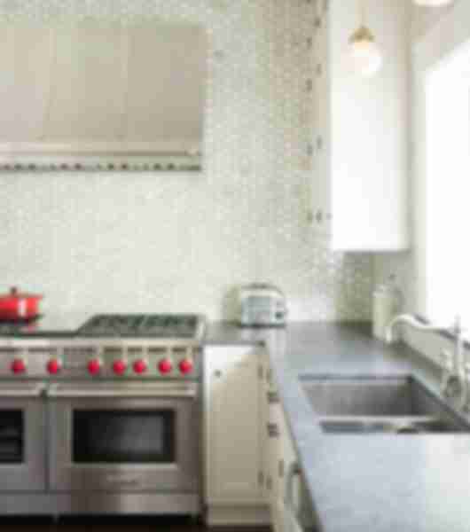 Silver stove with red nobs in front of white hexagon tile wall
