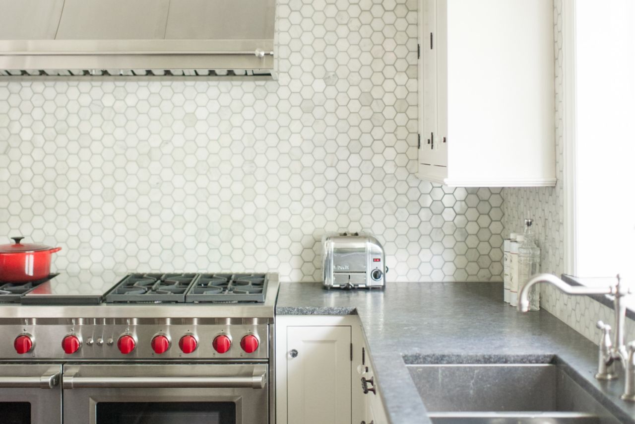 Silver stove with red nobs in front of white hexagon tile wall