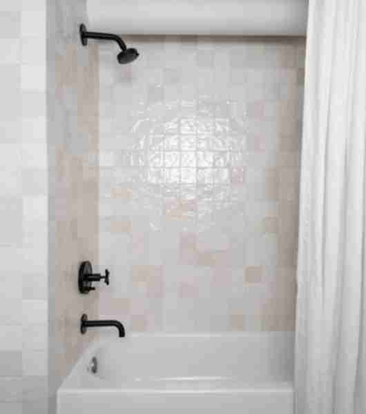 Cream-colored, handmade-look square ceramic tile adds varied tone and texture to the walls in this bathroom, and contrasts nicely with matte black shower fixtures.