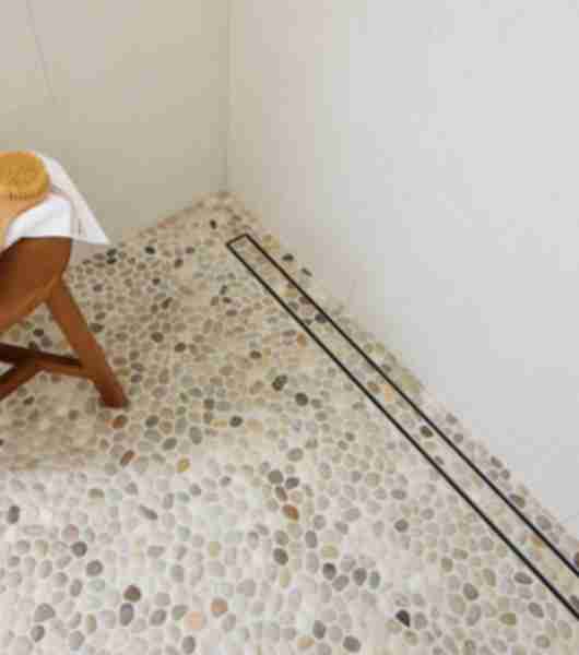 Overhead shot of pebble shower floor tile with small wooden stool