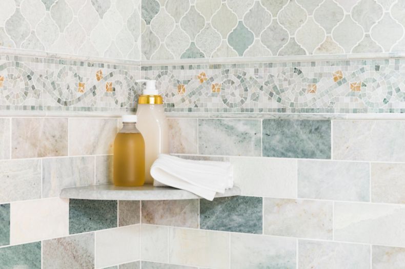 Corner of shower with green marble subway tile and mosaics on walls. 