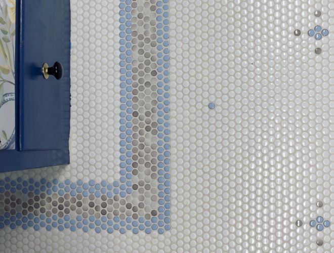 Overhead view of floor with white, blue and grey penny round tiles in a pattern with a border and repeated flower shapes.