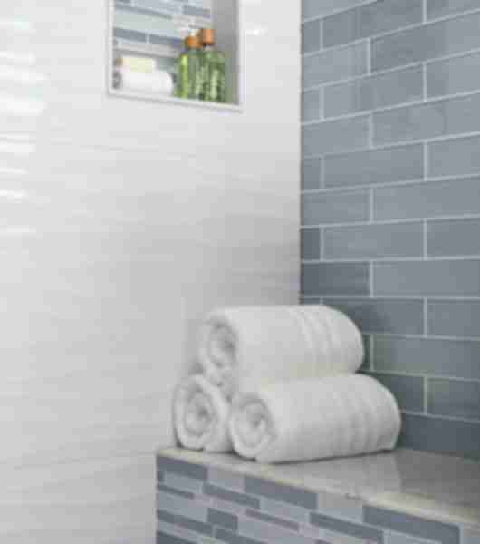Walk in shower with natural marble Ceramic and glass tiles in various shapes sizes and patterns.  Neutral whites greys makeup this color pallet for this space. Image features a detailed look at walls, bench and recessed niche.