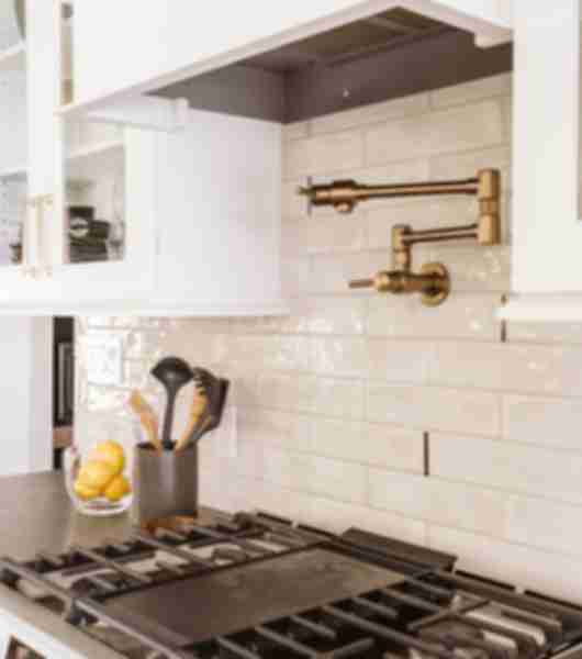 Elongated, handmade-look white subway tile is used on the backsplash over a gas stove. The tile is installed in a horizontal off-set pattern.