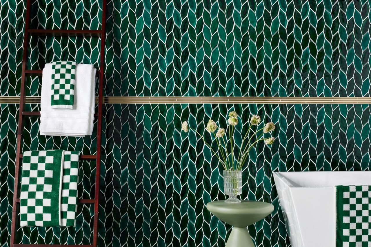 Green-leaf wall and floor tile with tub, towels and small green accent table with flowers.