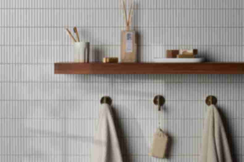 Bathroom wall tiled in long thin white tiles with a brown wood shelf holding toiletries