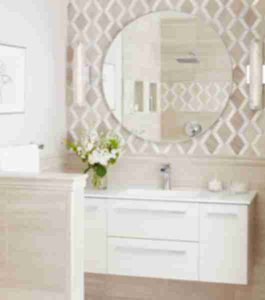 White bathroom vanity with white flowers. Circular mirror on beige and white tile wall.