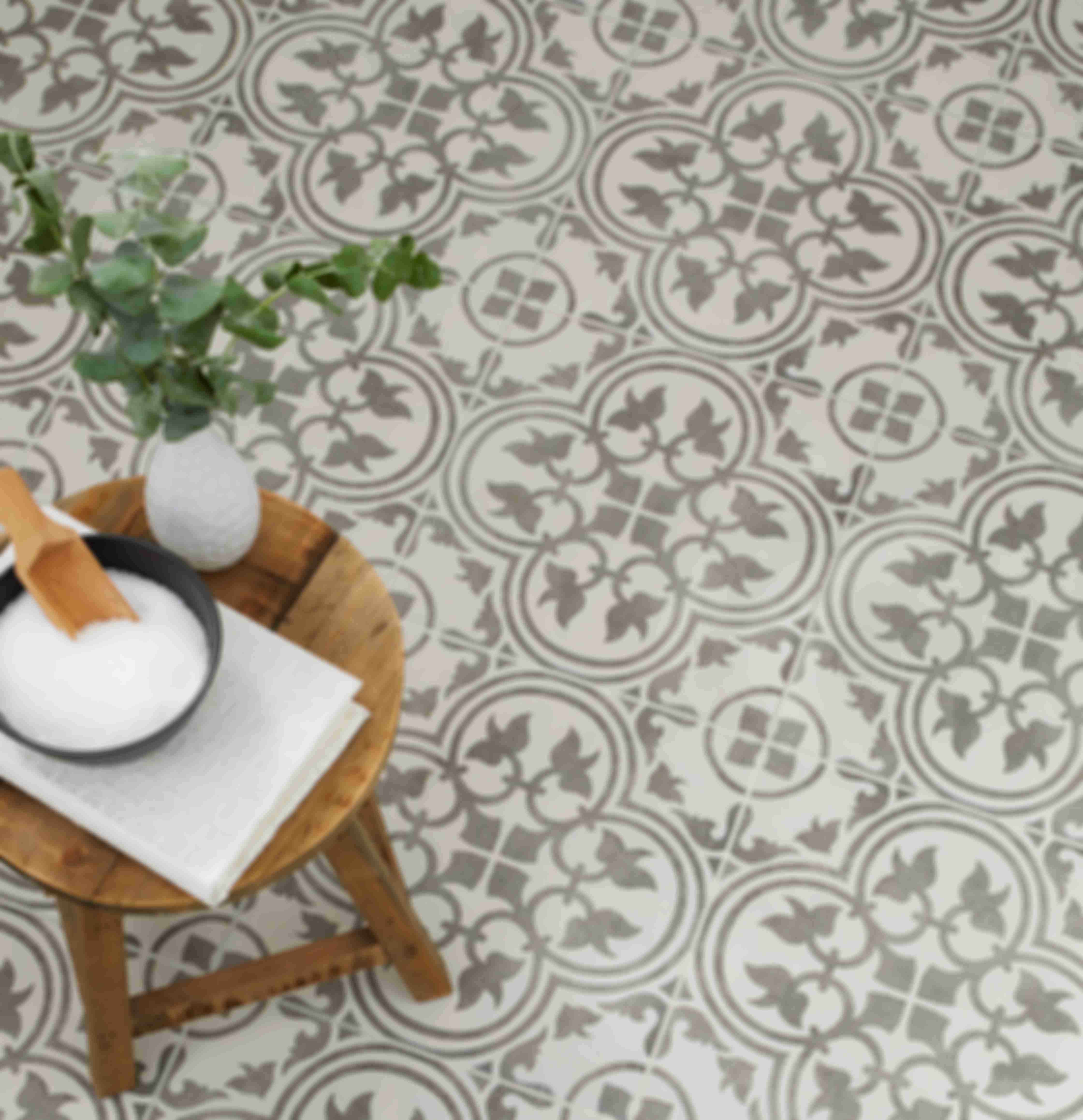 Tiled floor with a grey and white floral-inspired tile pattern and wood accent stool.