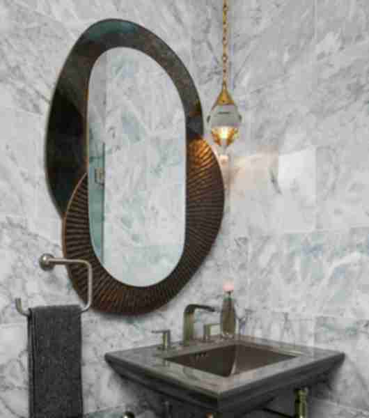 This bathroom features a sink positioned in the corner, where two walls covered in light gray polished marble tile meet. The tile is an oversized subway shape and the stone features white and gray veining.