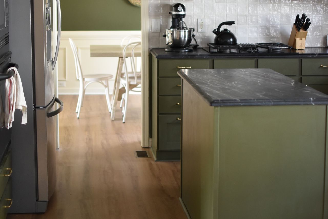 Green kitchen with brown, wood-look vinyl flooring