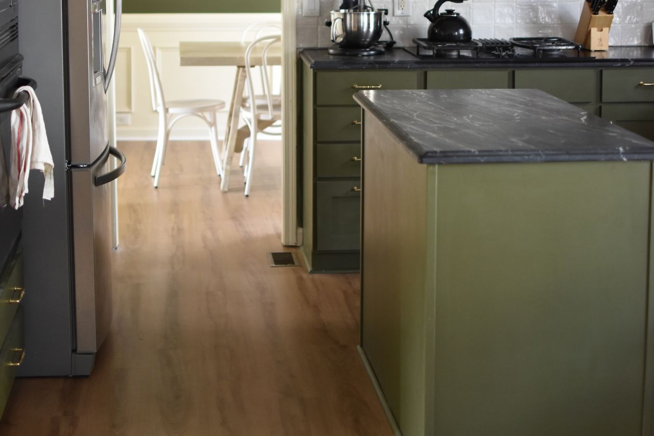 Green kitchen with brown, wood-look vinyl flooring