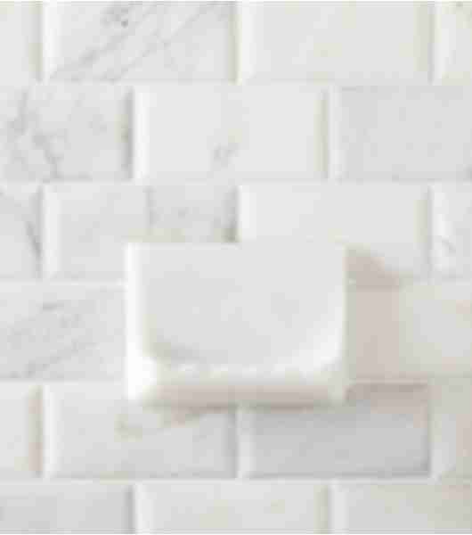 Shower wall with white marble subway tile and soap dish.