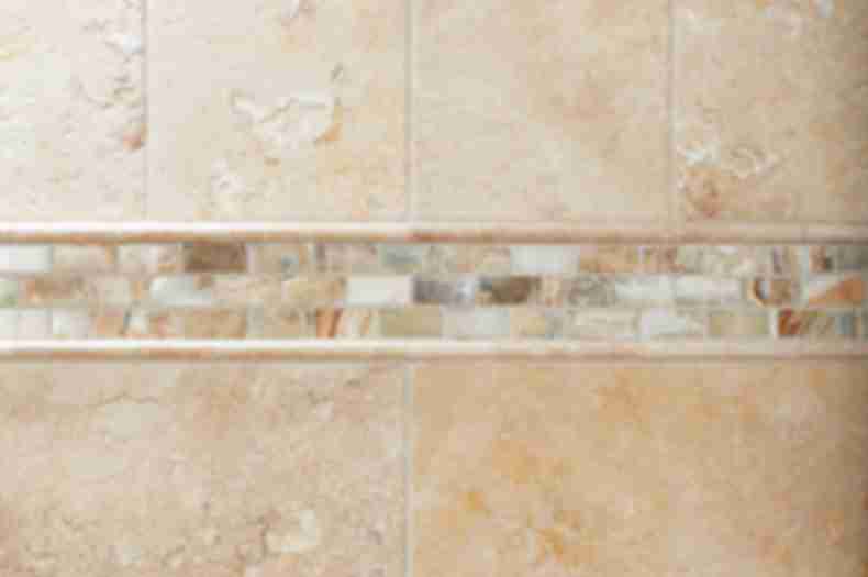Shower wall with beige tile, mosaic accent, and soap dish.