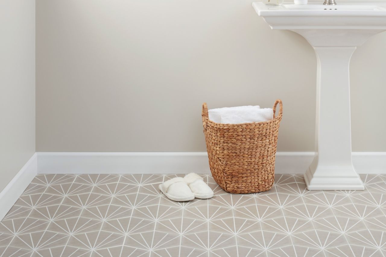 Bathroom with focus on hexagon floor tile lined with white for a pattern with in the tile.  White pedestal sink and wicker basket with slipper  and towels.