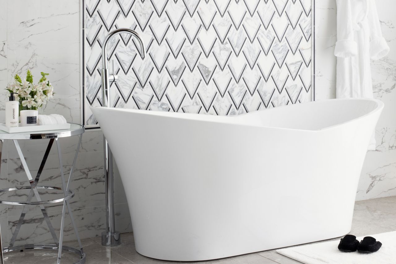Soaker tub with side table. Grey floor tile and black and white marble look on will with accent frame of patterned tile.