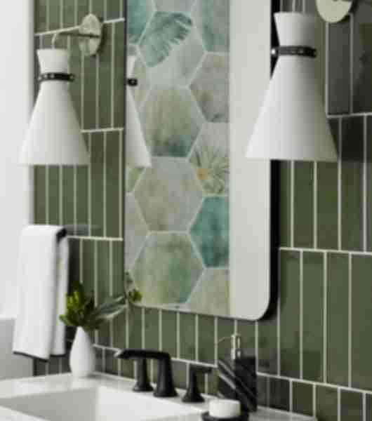 Sink with hand soap and small plant. White wall sconces and mirror on a green tile wall