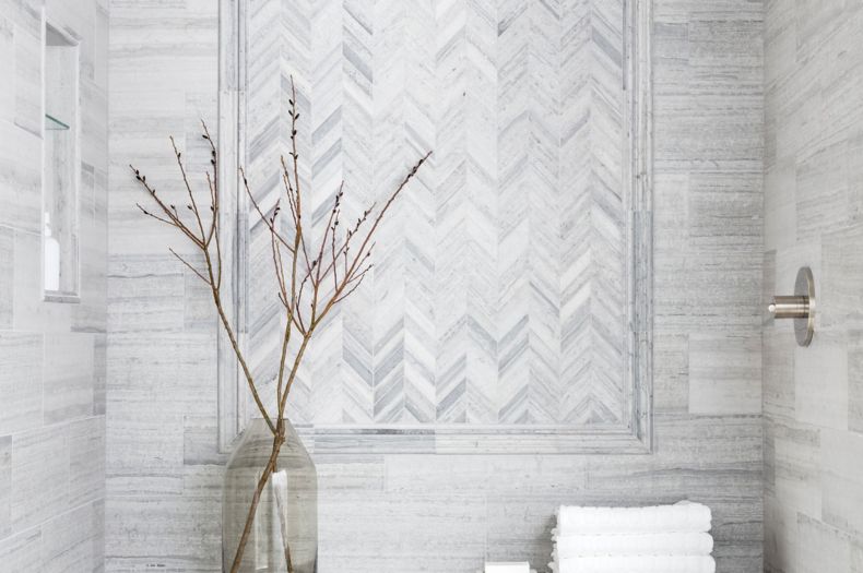 Sophisticated shower with grey limestone in chevron pattern with glass mosaic accents.