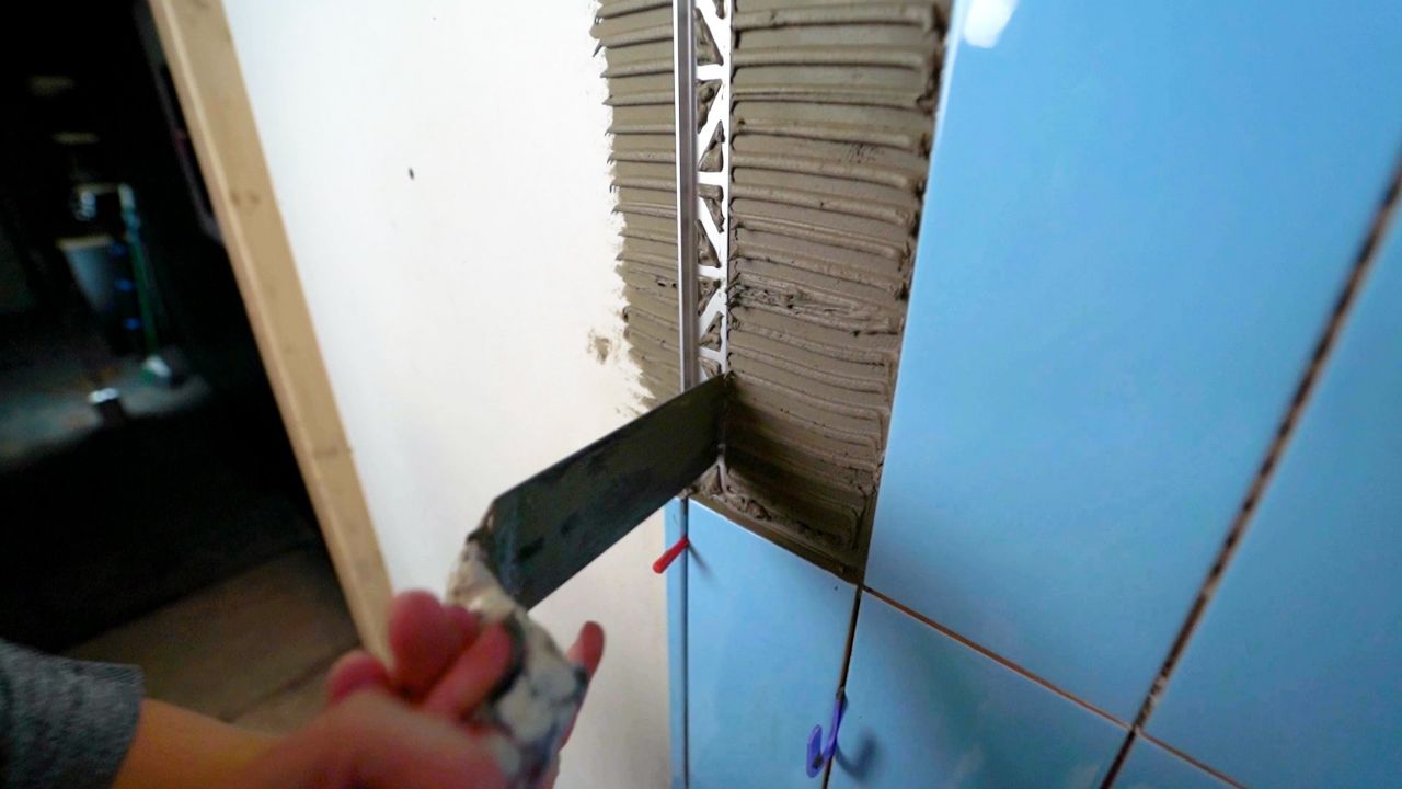 A person using a trowel to embed the leg of a piece of metal profile trim into thinset mortar. Tile will be installed on top of the embedded portion of the trim piece, and the leg holds the trim in place.