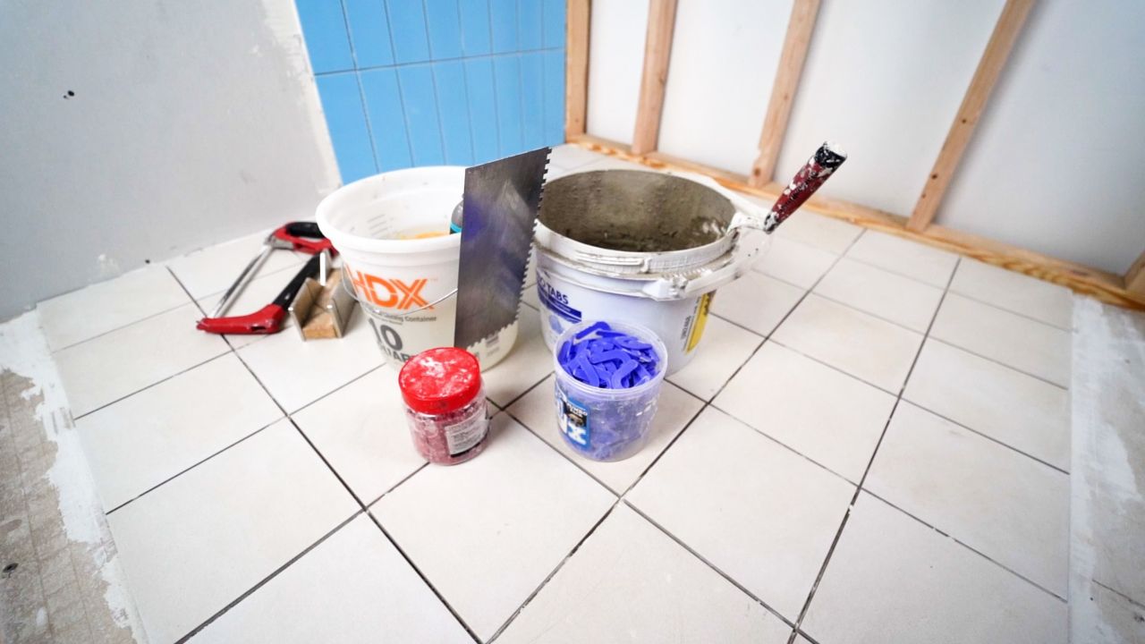 Materials and tools needed for finishing the edges of a tile installation. Items include a miter box and hacksaw, bucket of clean water and a sponge, bucket of thinset mortar, various trowels, and tile spacers and wedges.