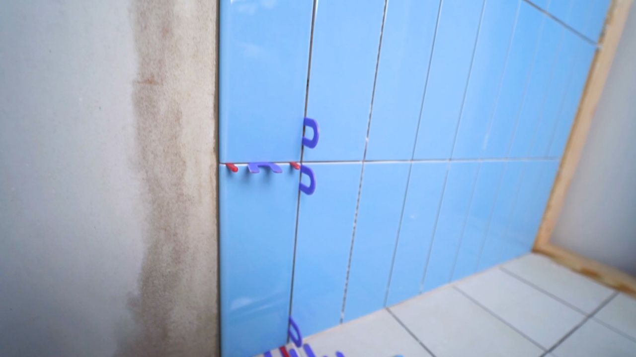 To create uniform grout joins, tile spacers and wedges are placed between blue tiles on a shower wall during a tile installation.