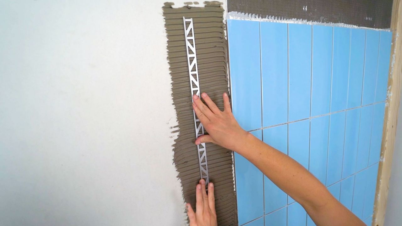 Applying pencil trim piece to wall, and embedding the leg of the trim piece into the thinset mortar below. The tile will be installed on top of this piece.