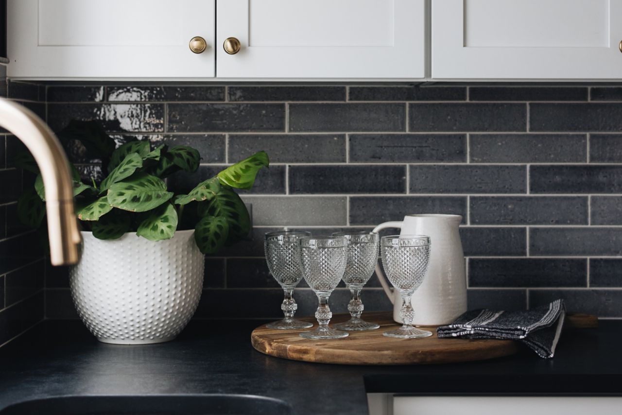 A kitchen backsplash with dark grey tile and contrasting white grout.