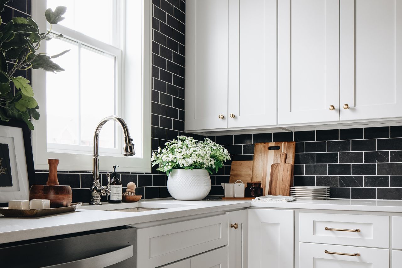 Kitchen with black tile wall and white cabinetry.