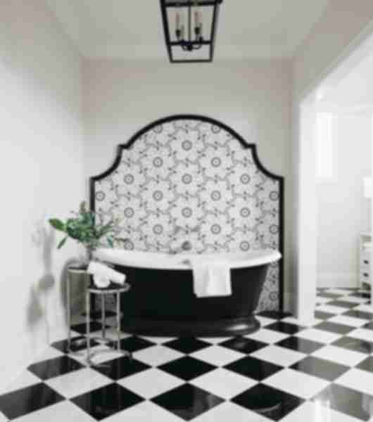Bathroom with black and white checkerboard floor tile and a black and white mosaic accent wall. Bathtub and small table with a plant.