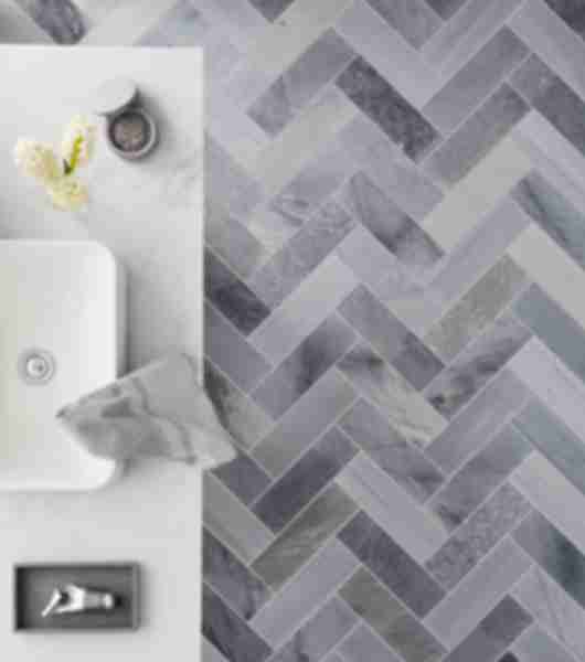 Bathroom floor tile laid in a herringbone with natural marble and a aerial view of a vessel sink