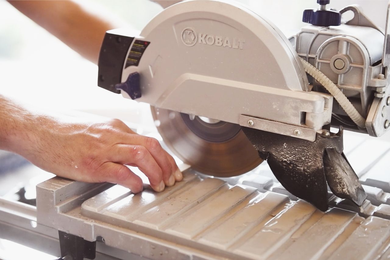 Using a wet saw to cut white subway tiles to the correct size before installing tiles in a kitchen backsplash.