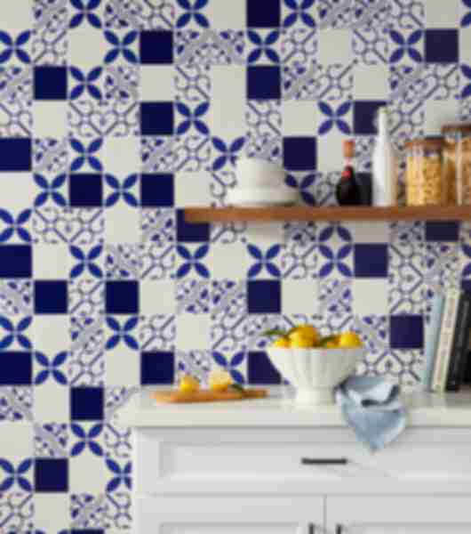 Blue patterned tile kitchen wall with white counter, floating shelf and bowl of fruit.