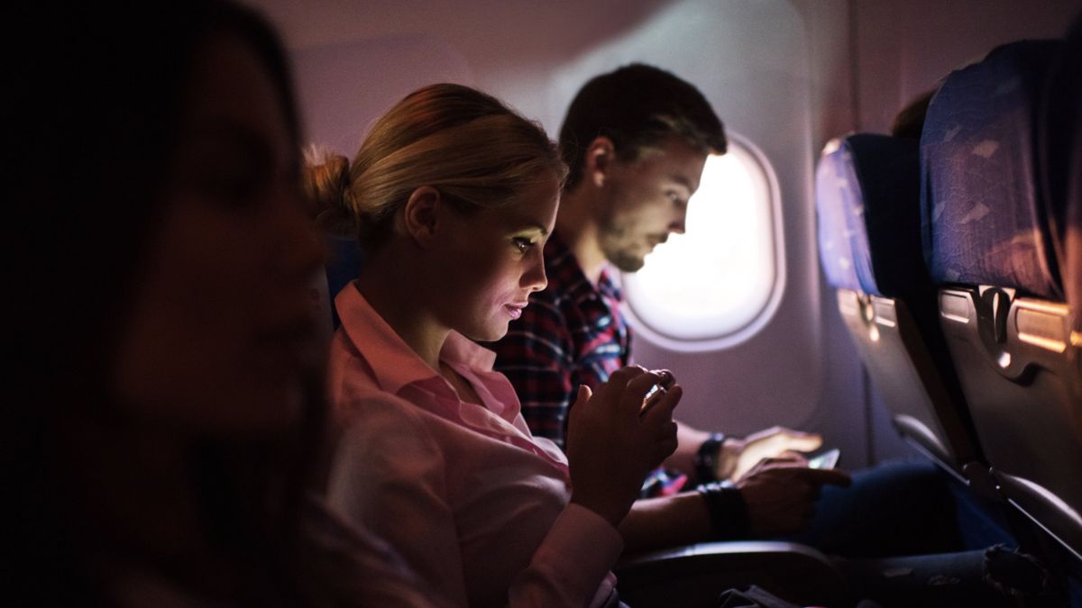Two people sitting on an airplane use their mobile devices.