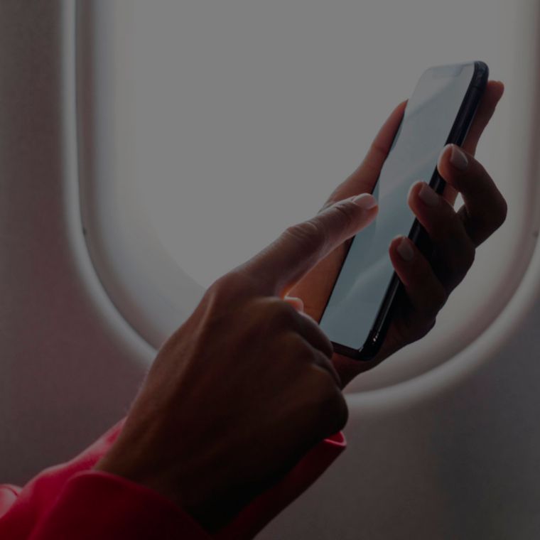 A person uses a mobile phone while sitting next to an airplane window.