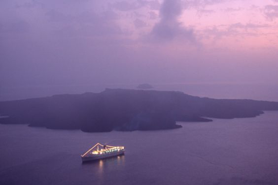 一艘游轮的鸟瞰图，甲板和索具上都有灯光, 在一个遥远的岛屿前面的海面上.
