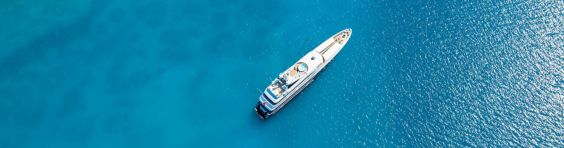 An overhead view of a large private yacht in a bright blue sea.