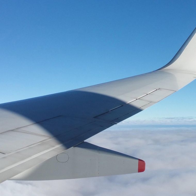 The wing of a private jet above the clouds against a blue sky.