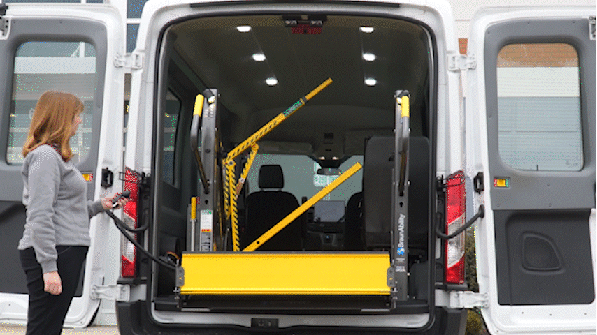 Wheelchair user approaching DPA lift with LiftSentinel and attendant. 