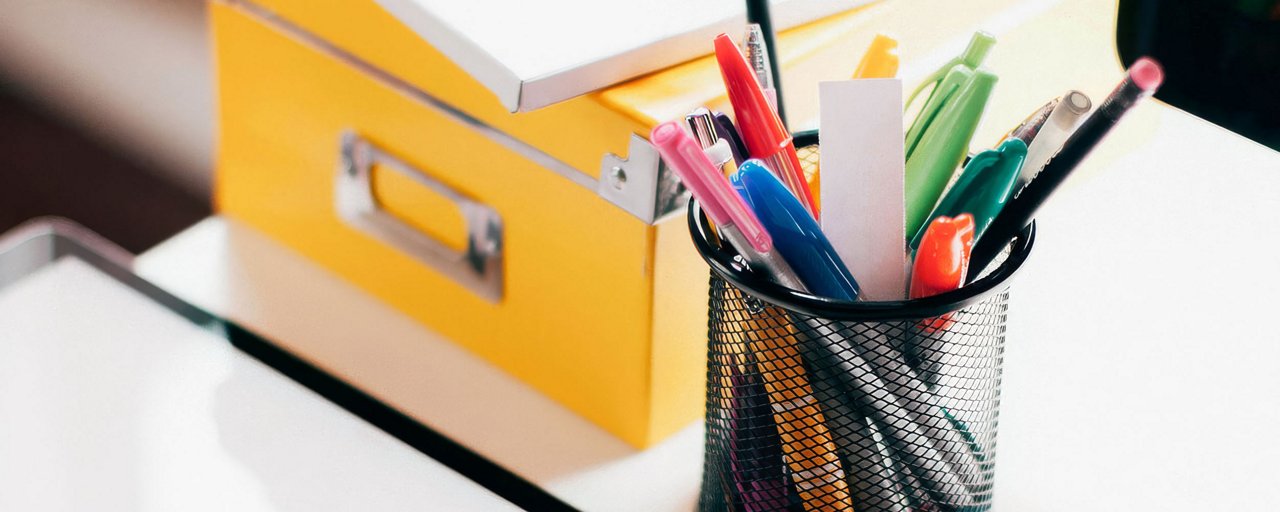 A cup of colorful pens and a yellow box on a desk 