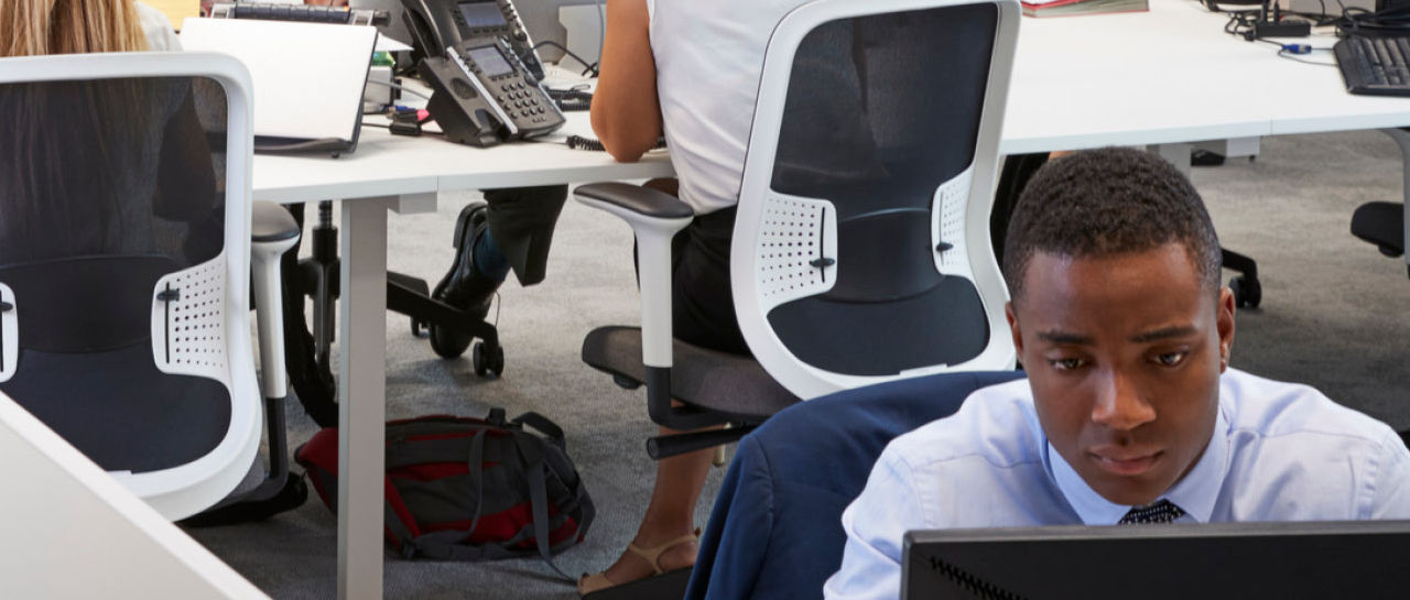 A businesswoman leads a team meeting in the office, showcasing data on a computer to her fellow businesspeople.
