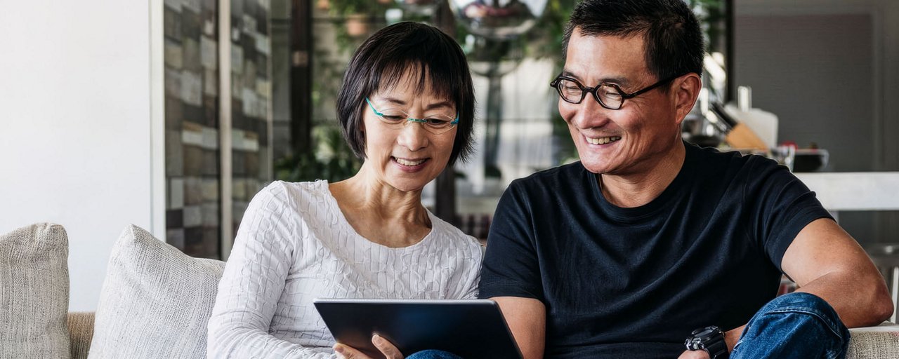 A man and woman looking at a tablet together on the couch
