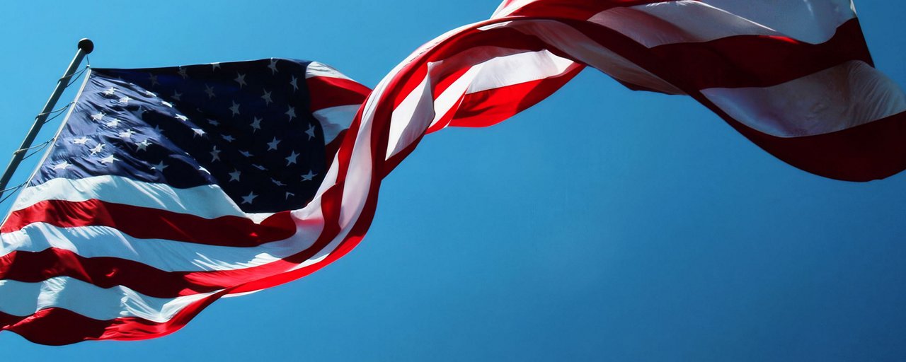 A large American flag blowing in the wind against a clear blue sky