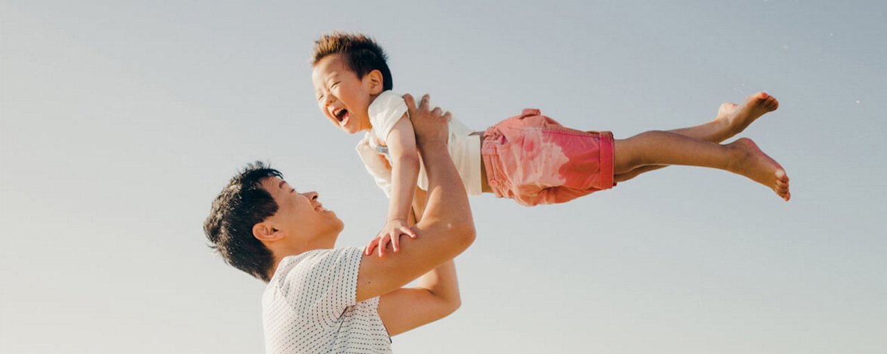 A father laughing and swinging his young son into the air on the beach 