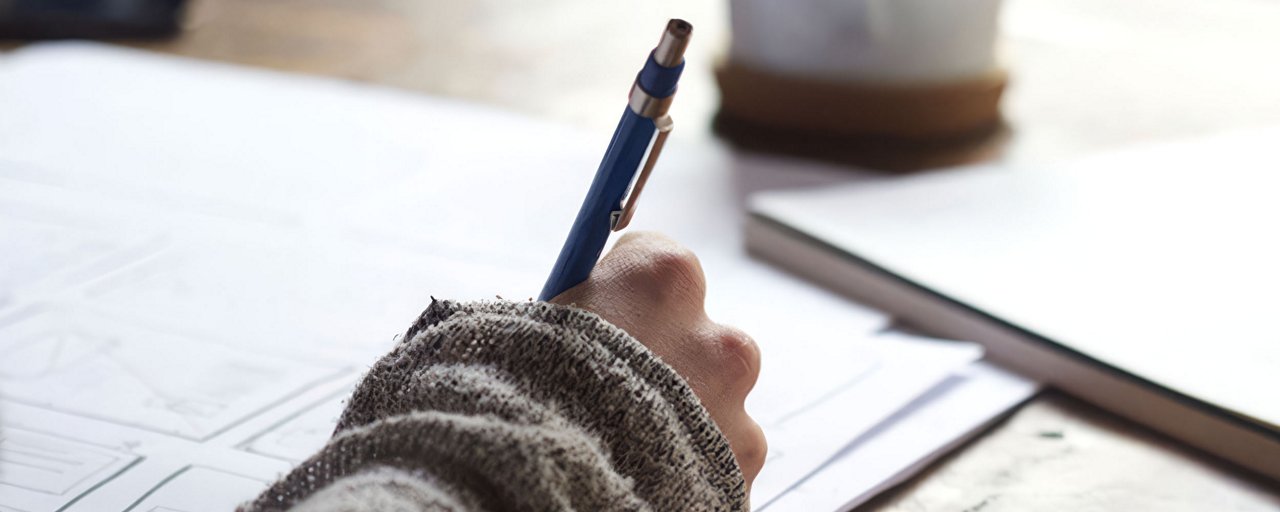 Woman taking notes with a pen at a wooden table