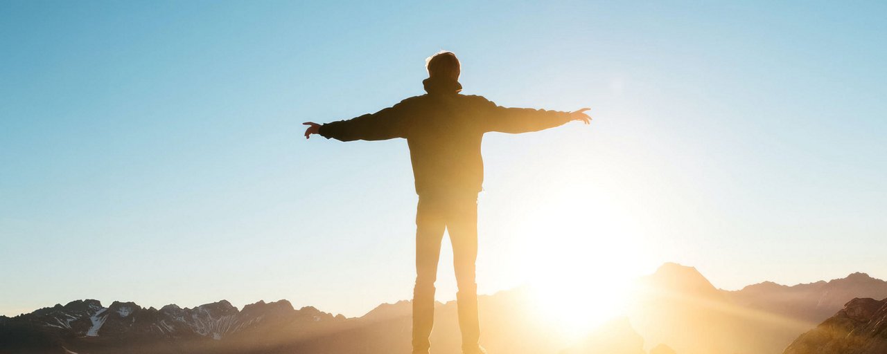 Man standing on the top of a mountain arms raised out and greeting the sunrise