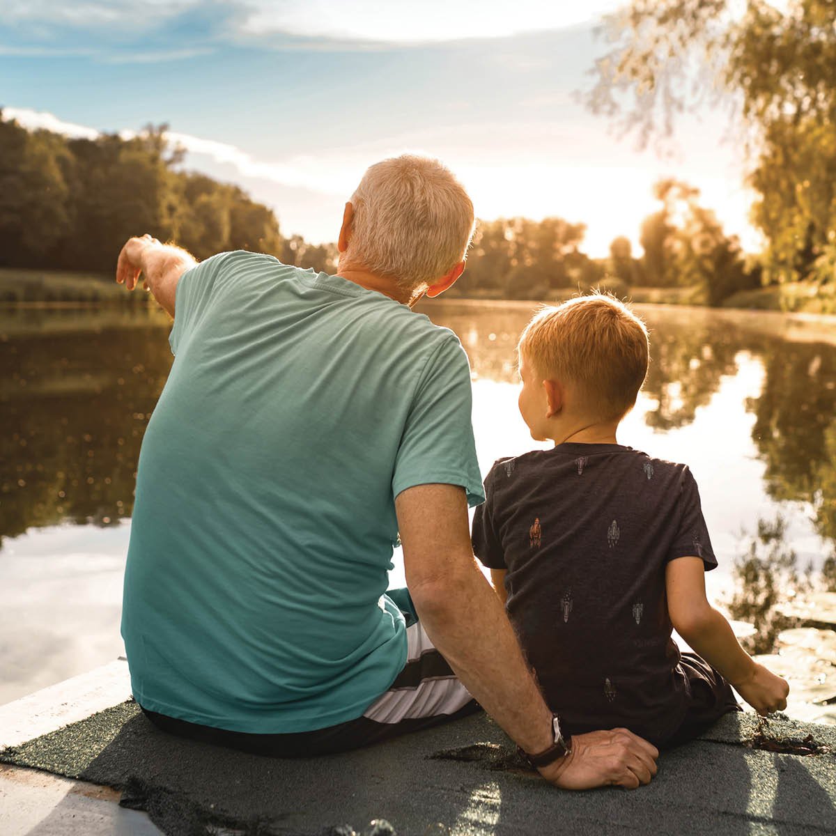 Two people sitting together at the edge of a boat, looking across a calm lake at sunset.