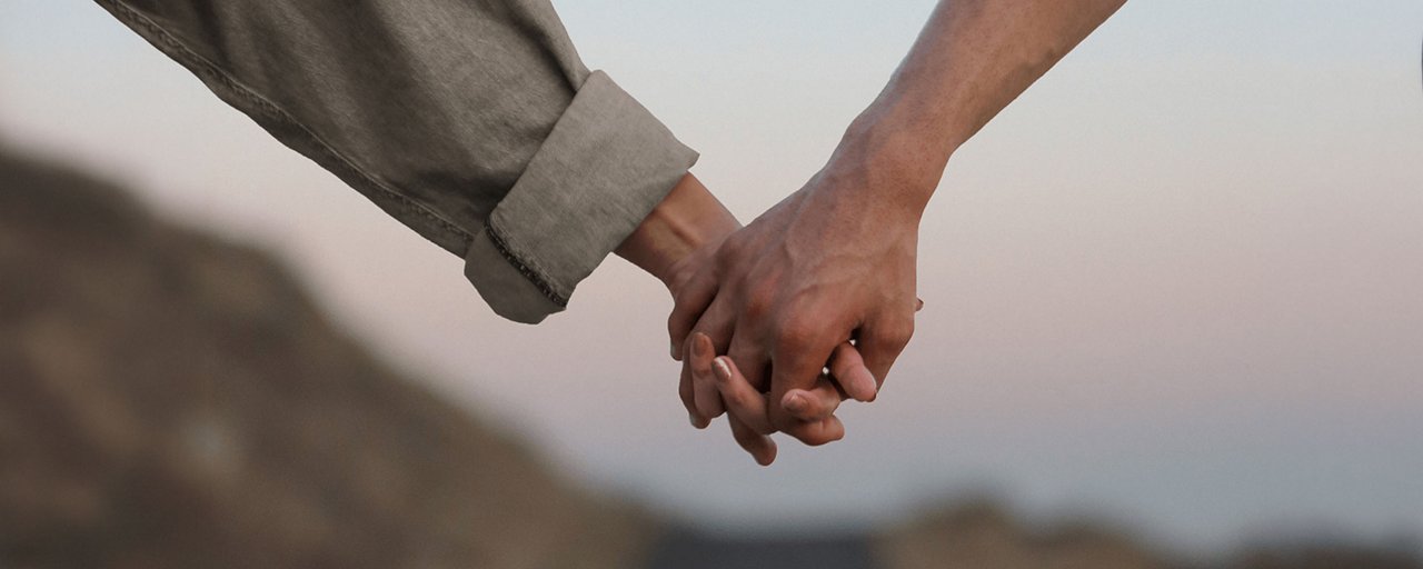 Close up of a man and woman holding hands and walking down a dirt road