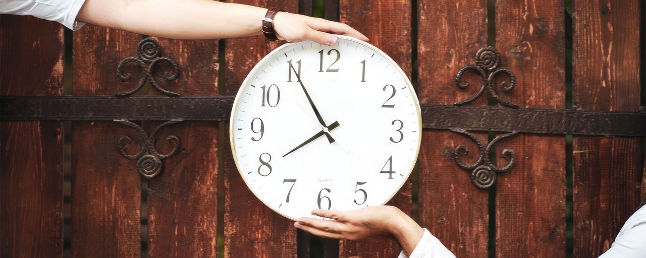 Two people holding up a white clock in front of antique wooden doors