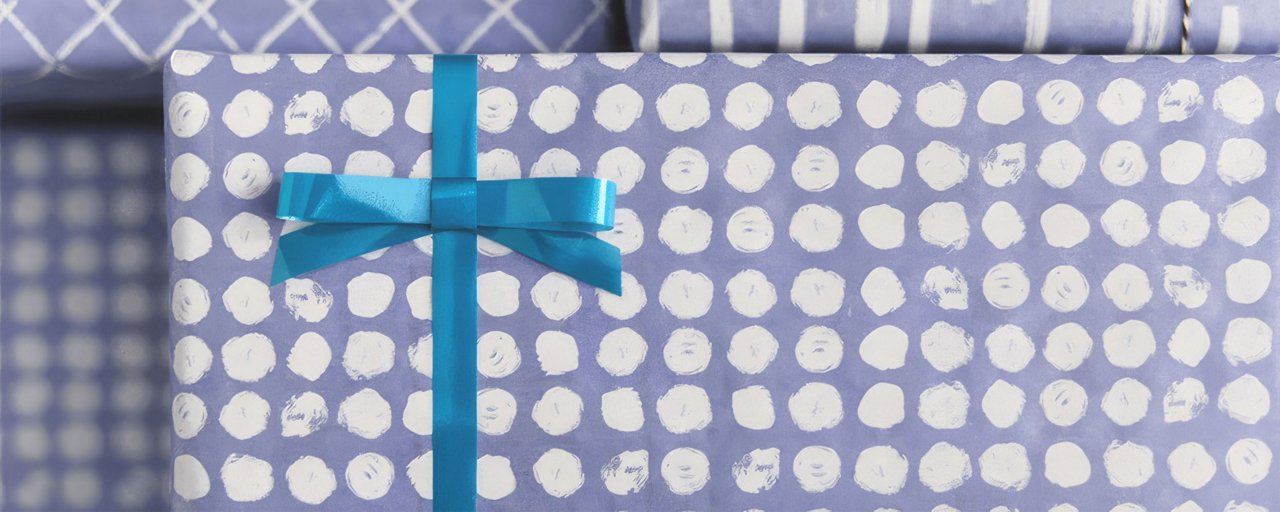 Close up of a present wrapped in purple polka dot wrapping paper with a blue bow