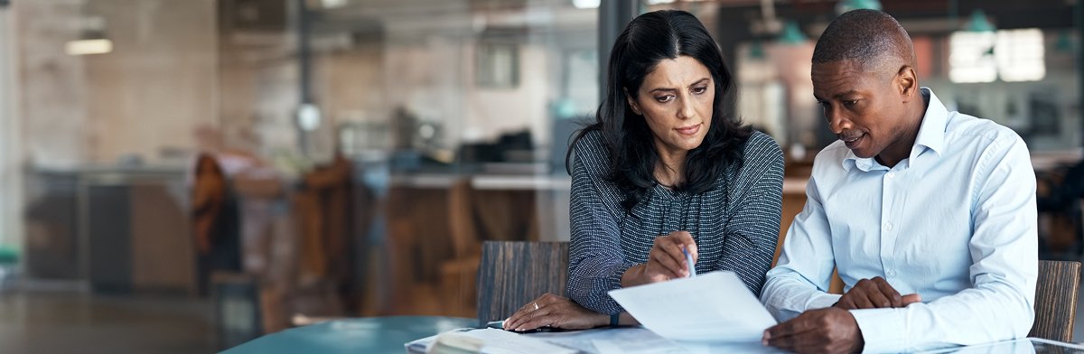 A man and woman seated at a table, reviewing documents and discussing details together.