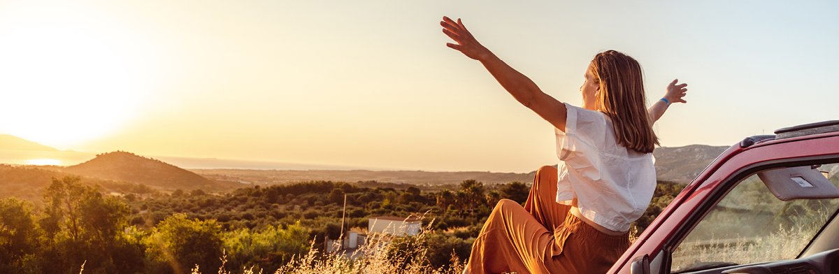 Une femme prospère irradie de bonheur et de liberté en pleine nature, célébrant l'été devant un paysage de ciel et de montagnes.